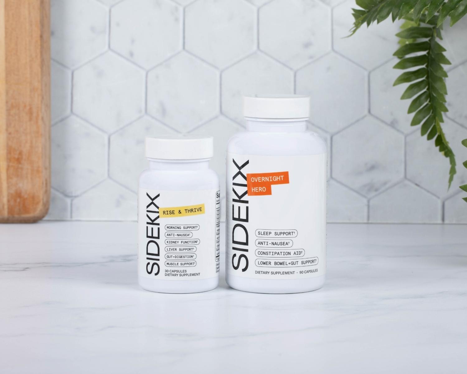 Two bottles of Sidekix Dietary Supplements on kitchen counter. Rise & Thrive lists morning support†, anti-nausea†, kidney function†, liver support†, gut+digestion†, muscle support†, 30 capsules. Overnight Hero lists sleep support†, anti-nausea†, constipation aid† and lower bowel+gut support†, 90 capsules. 